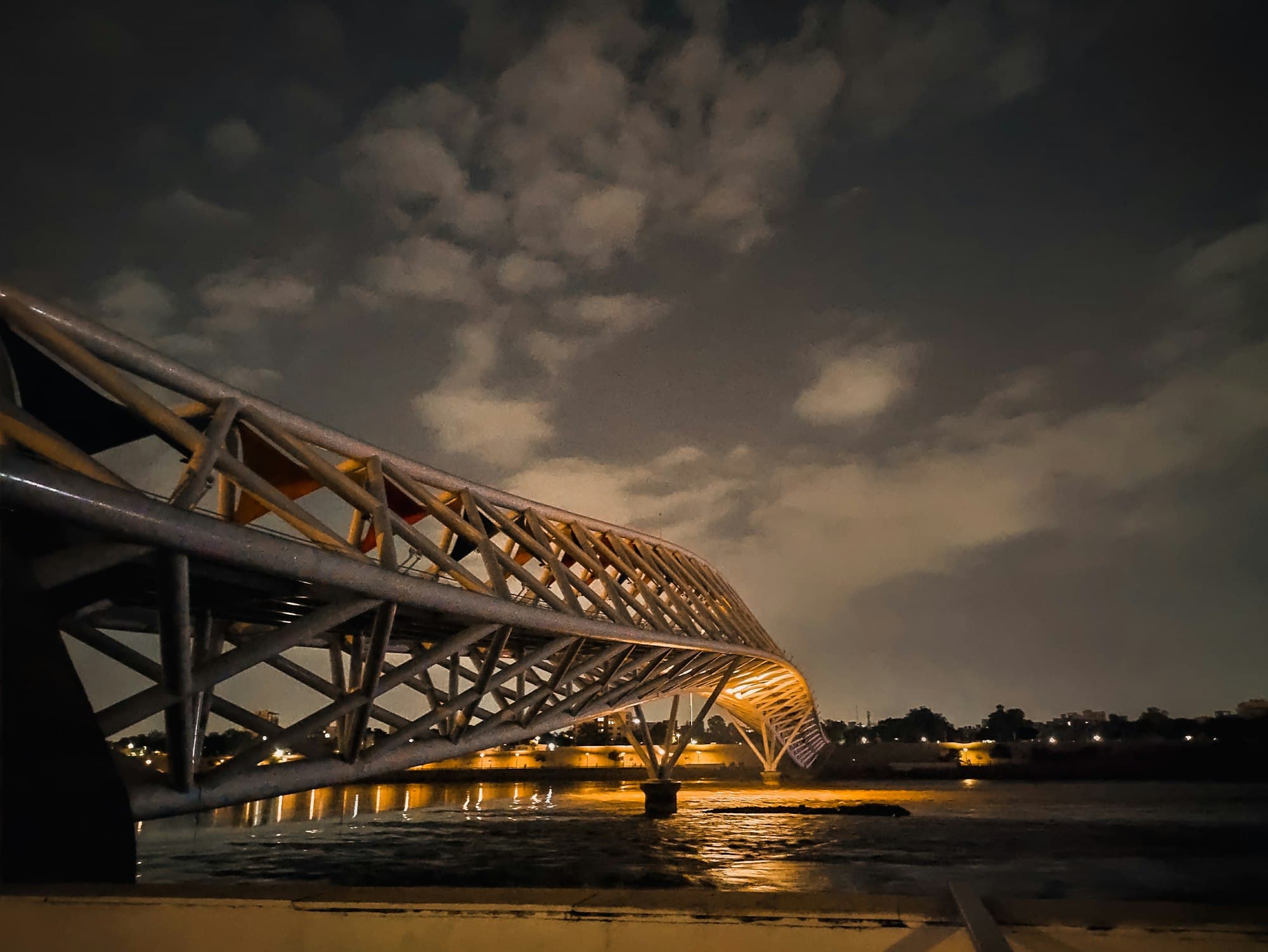 Atal Bridge over the Sabarmati at night, its steel canopy lit warm orange